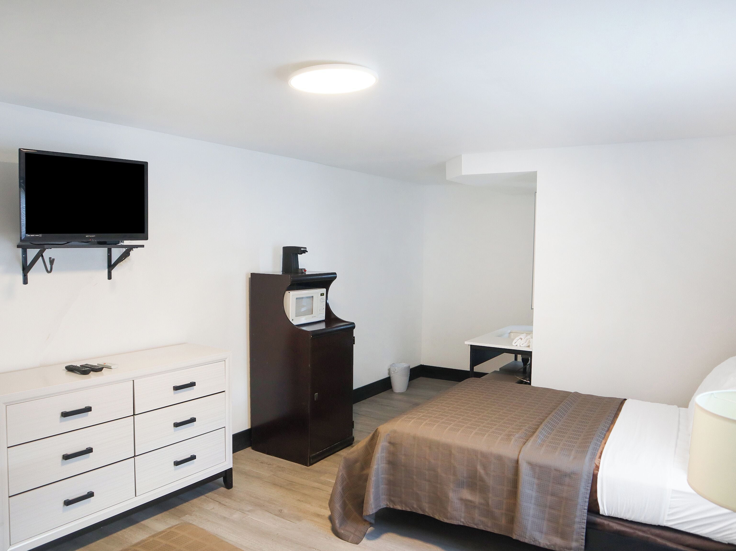 Habitación de hotel con cama, televisor montado en la pared, cómoda y microondas en un mueble.