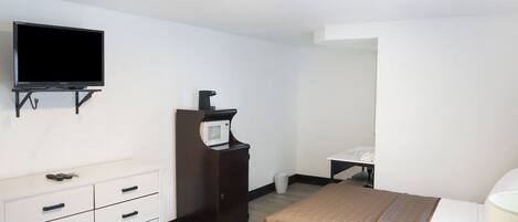 Habitación de hotel con cama, televisor montado en la pared, cómoda y microondas en un mueble.