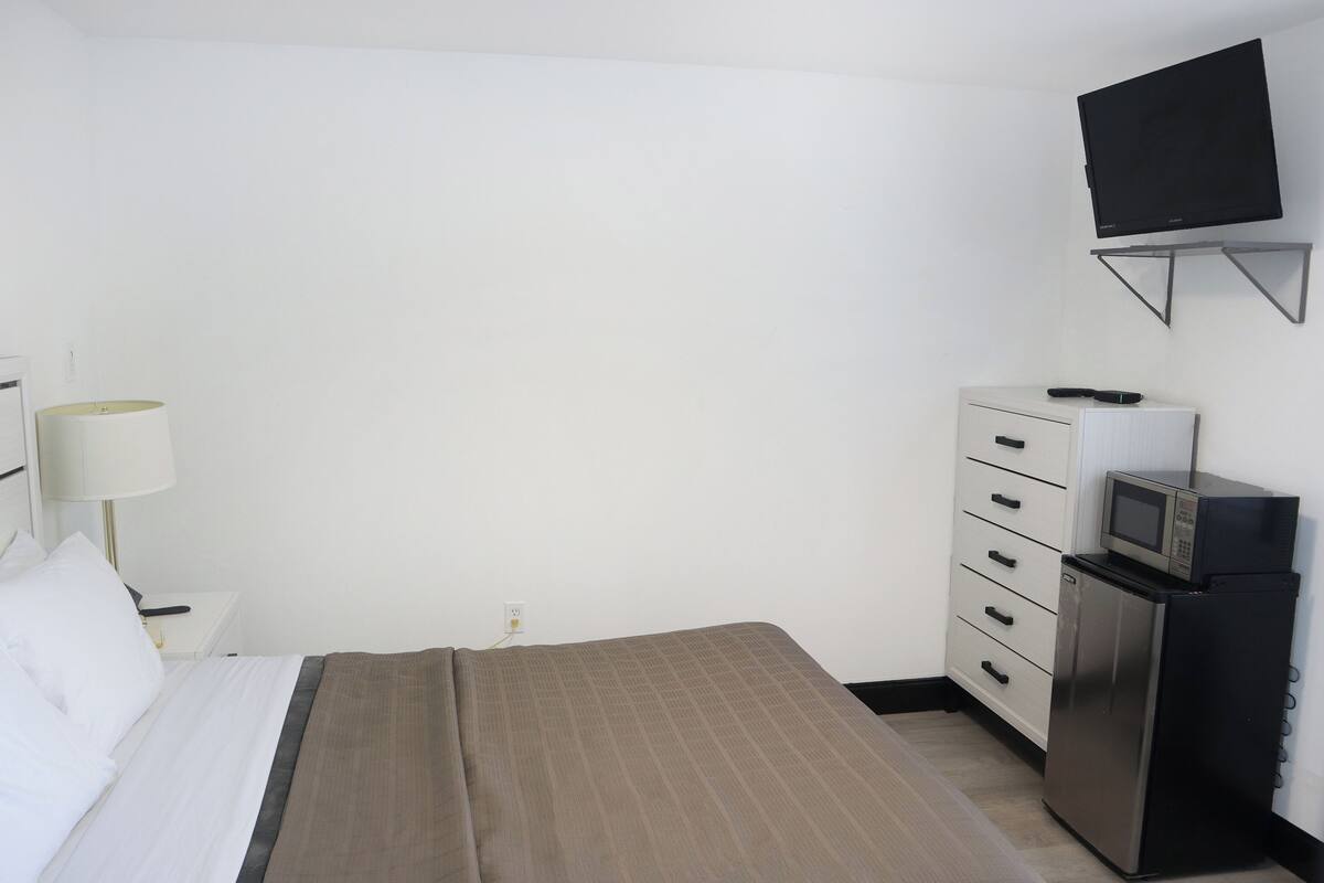 Une chambre d’hôtel équipée d’un lit, d’un bureau, d’une lampe, d’une télévision et d’un mini-bar.