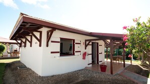 A small, single-story building with a white exterior and brown accents, featuring a covered patio area with outdoor seating. - Jéricho Gîtes & Spa (Capesterre-de-Marie-Galante)