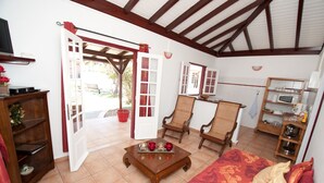 A cozy living room with a wooden coffee table, a sofa, and a dining area with a microwave and shelves. - Jéricho Gîtes & Spa (Capesterre-de-Marie-Galante)