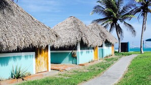 A row of thatched-roof huts with a concrete pathway leading to them. - Azul Surf Club (El Cuco)