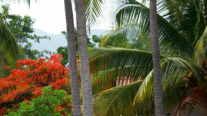 A tropical setting with thatched-roof huts, palm trees, and a red flowering tree. - Azul Surf Club (El Cuco)