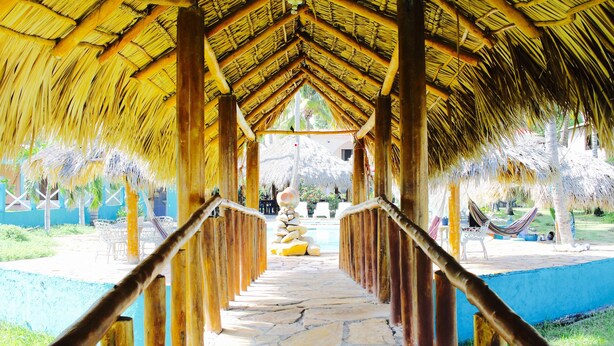 A thatched-roof corridor leading to a pool area with lounge chairs and a hammock. - Azul Surf Club (El Cuco)