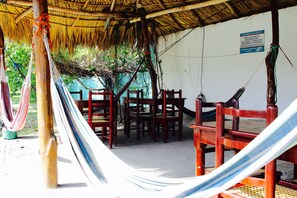 Un espace extérieur doté d’un toit de chaume, de chaises en bois et d’un hamac.