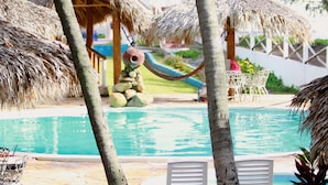 A pool area with a slide, thatched-roof structures, and palm trees. - Azul Surf Club (El Cuco)