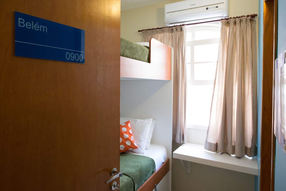 A hotel room with a bunk bed, a window with curtains, an air conditioning unit, and a sign indicating room number 0900.