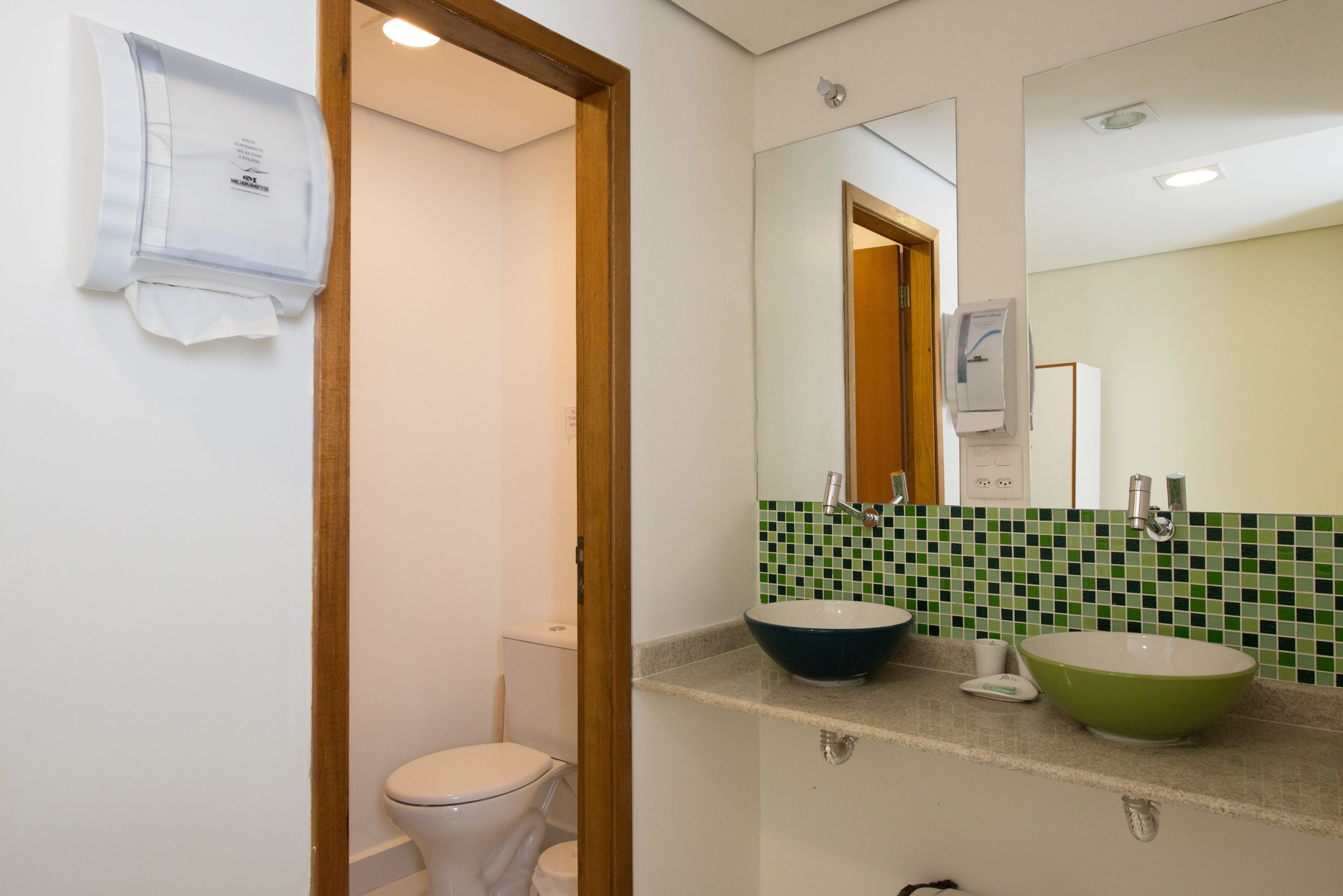 A bathroom with a toilet, a sink with a green basin, a mirror, and a towel hanging on the wall.