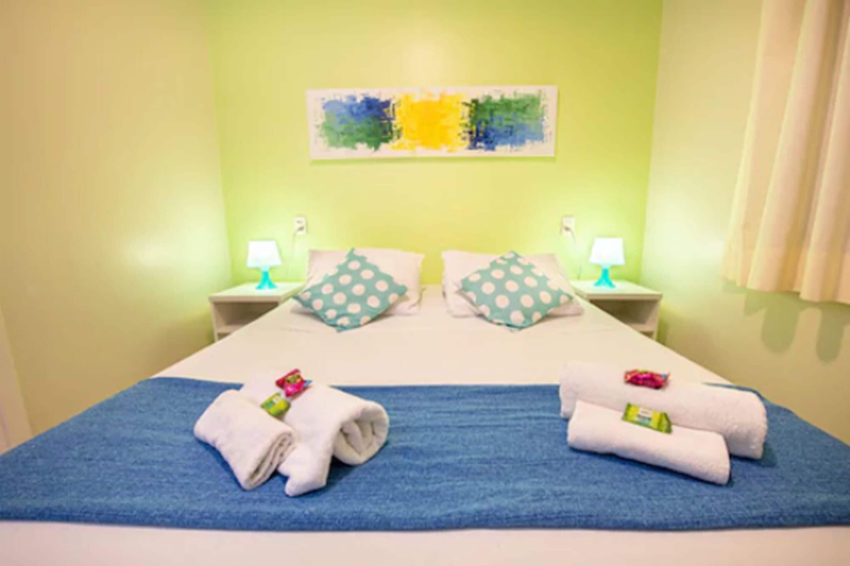 Habitación de hotel con cama, dos mesitas de noche, un cuadro en la pared y toallas sobre la cama.