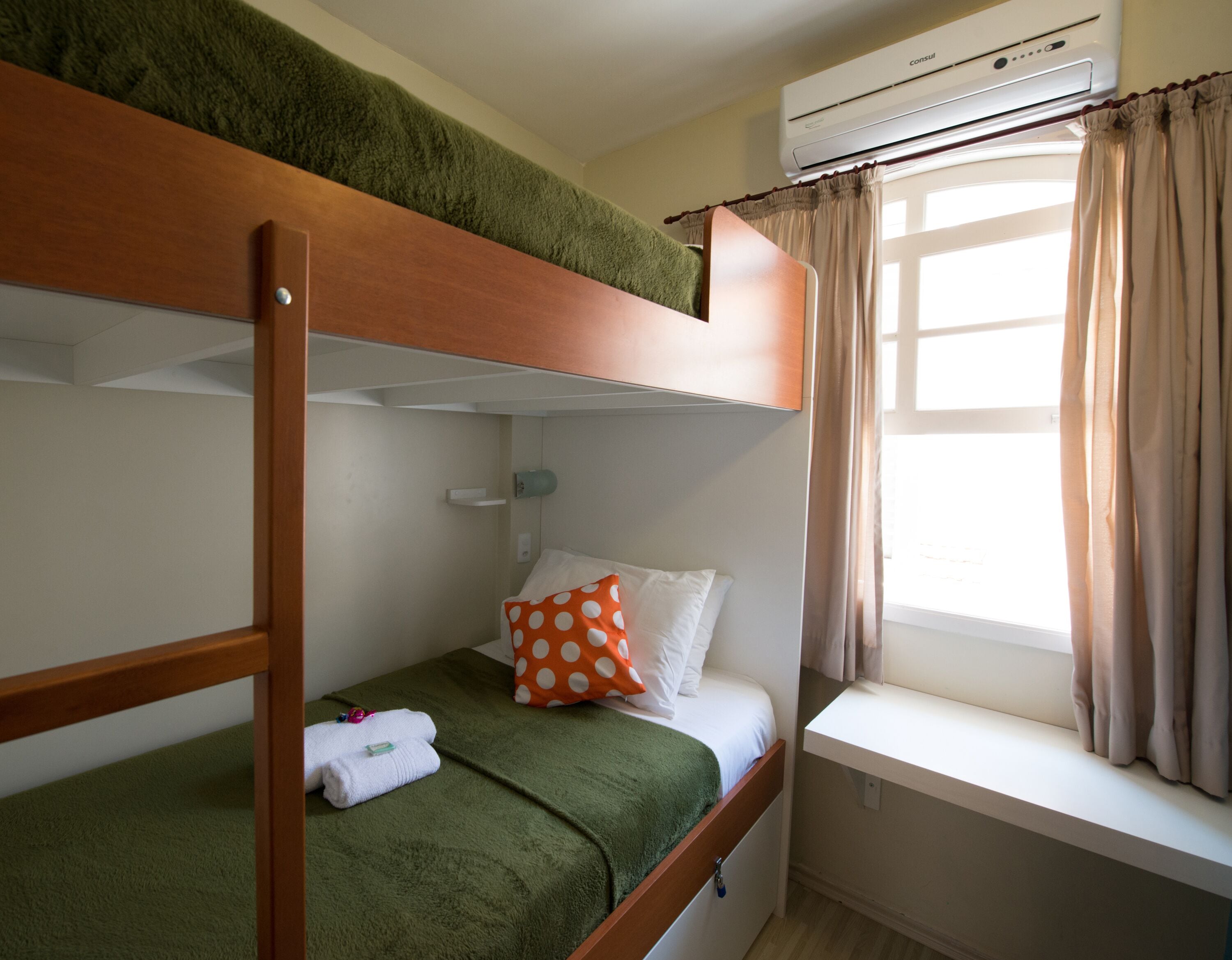 A bunk bed room with a window, curtains, and an air conditioning unit.