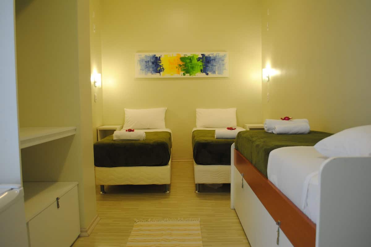 A hotel room with two beds, a small cabinet, a painting on the wall, and a light switch.