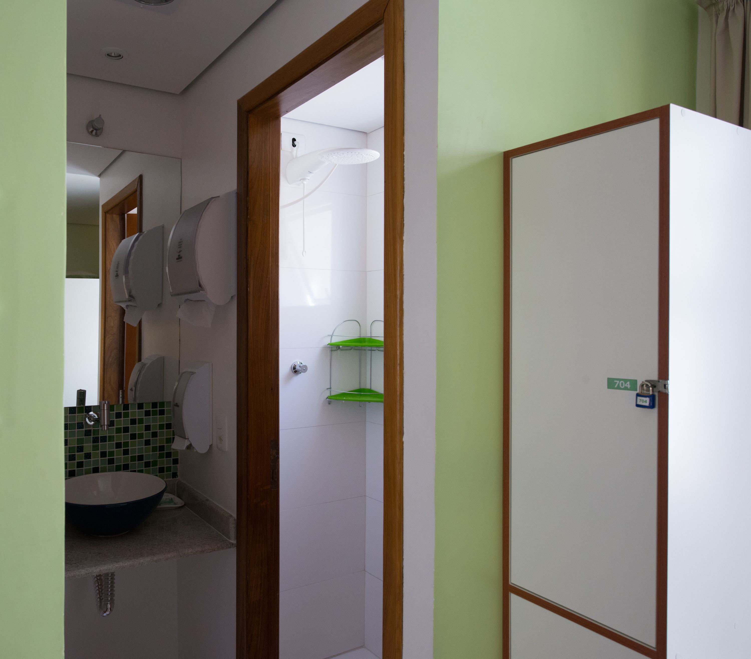 Un bagno con il water, un lavandino e uno specchio. Si nota uno scaffale verde e un armadietto bianco.