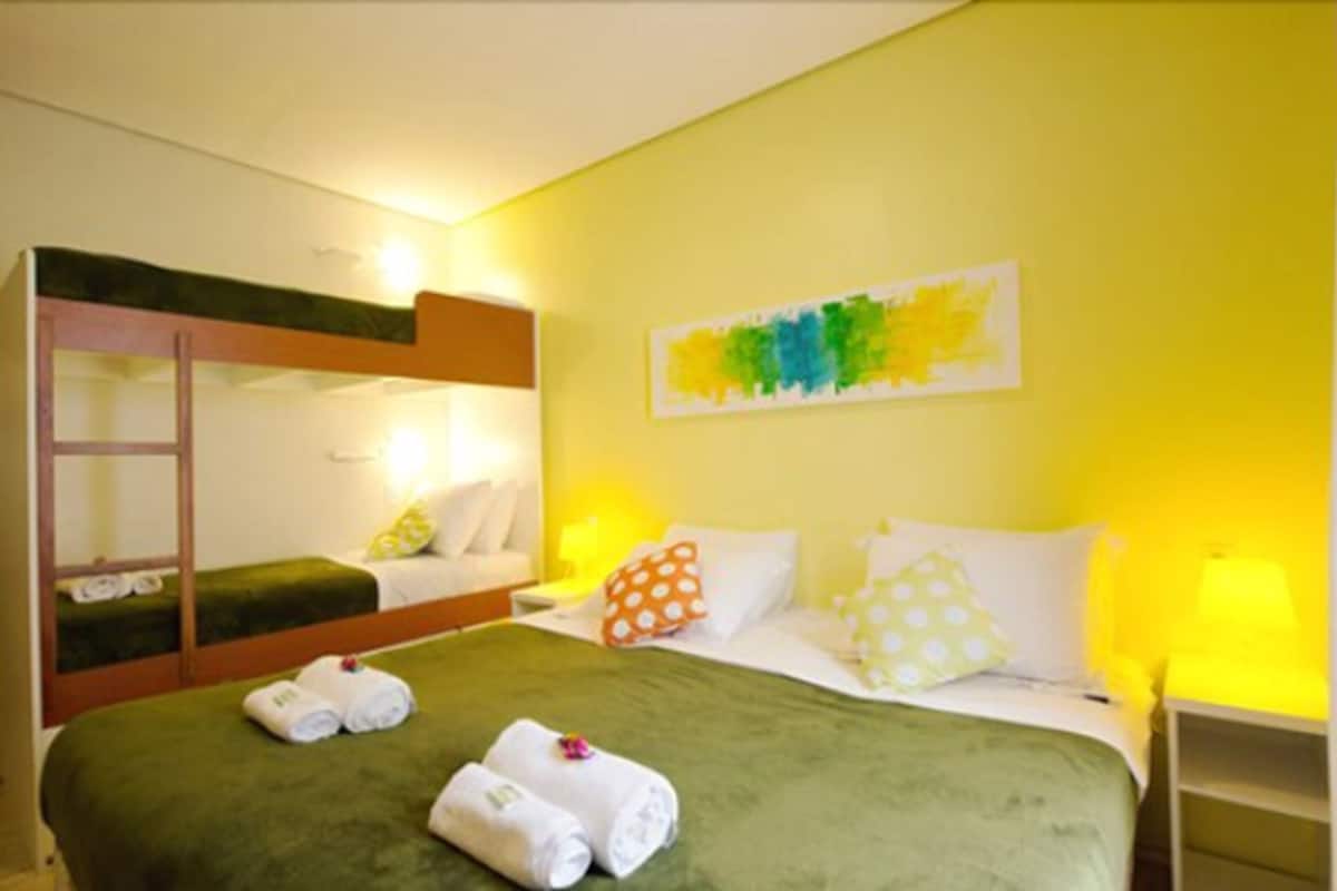 A hotel room with bunk beds, a green bedspread, and a colorful abstract painting on the wall.