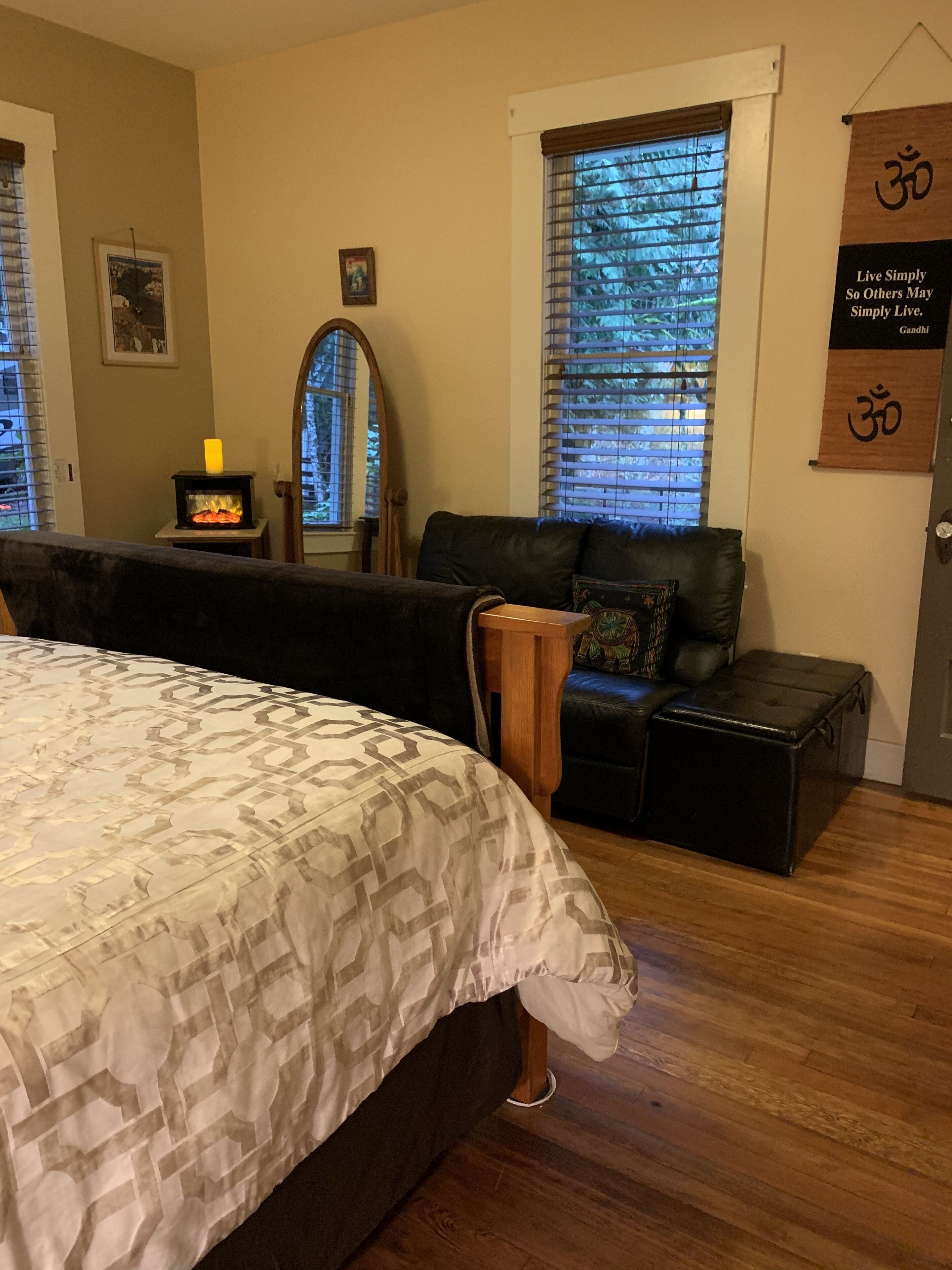 A bedroom with a bed, a sofa, a bench, a fireplace, and a window with blinds.