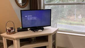 Quarto com televisão em suporte de madeira, lareira, janela com vista para árvores e espelho na parede.