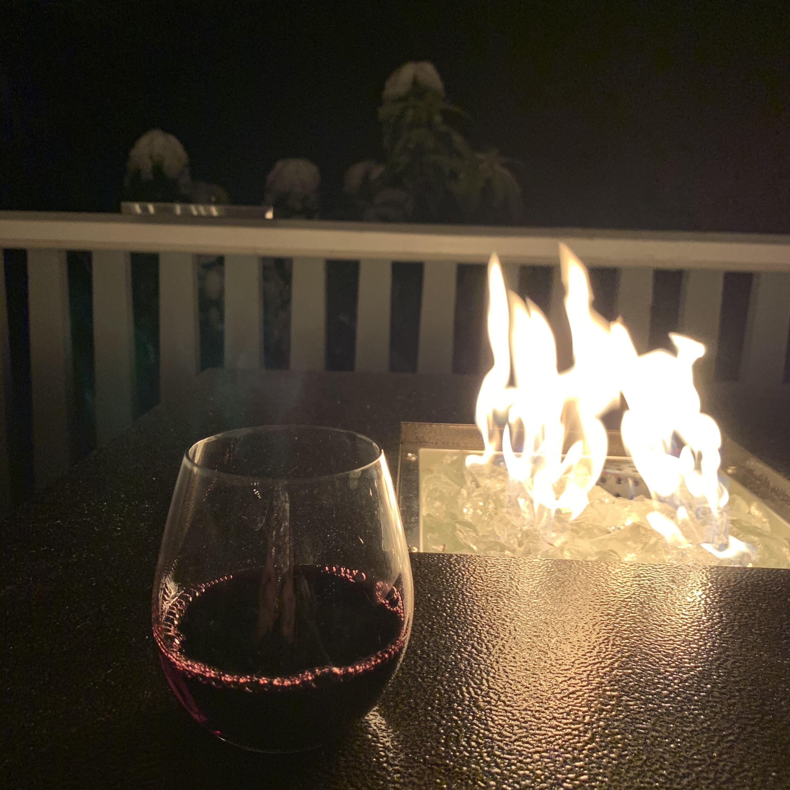 A glass of red wine on a table with a fire feature in the background.