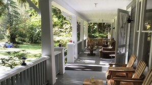 Varanda coberta com cadeiras e mesa de madeira, com vista para um jardim.