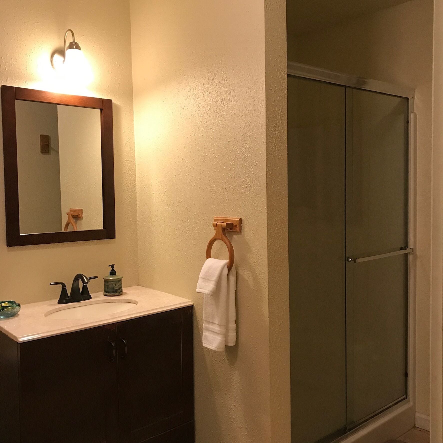 A bathroom with a sink, mirror, towel rack, and a shower door.