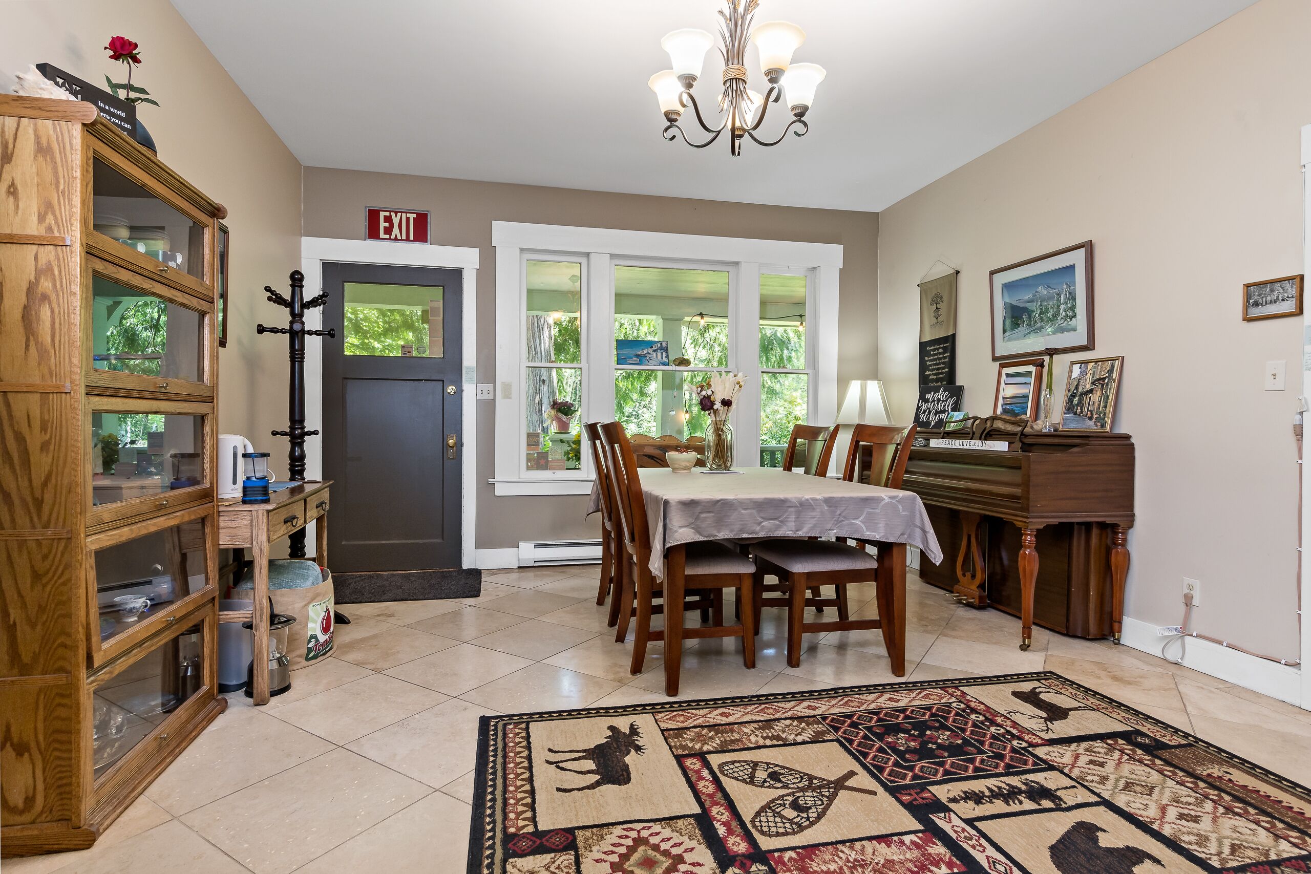 A dining area with a table, chairs, a chandelier, and a view through large windows.