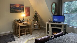 Um quarto acolhedor com uma mesa de jantar, uma pequena árvore de Natal, uma lareira e uma grande janela com vista para a floresta.
