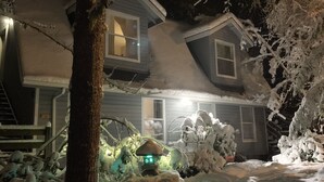 Uma casa de dois andares com telhado coberto de neve e uma janela visível no segundo andar.