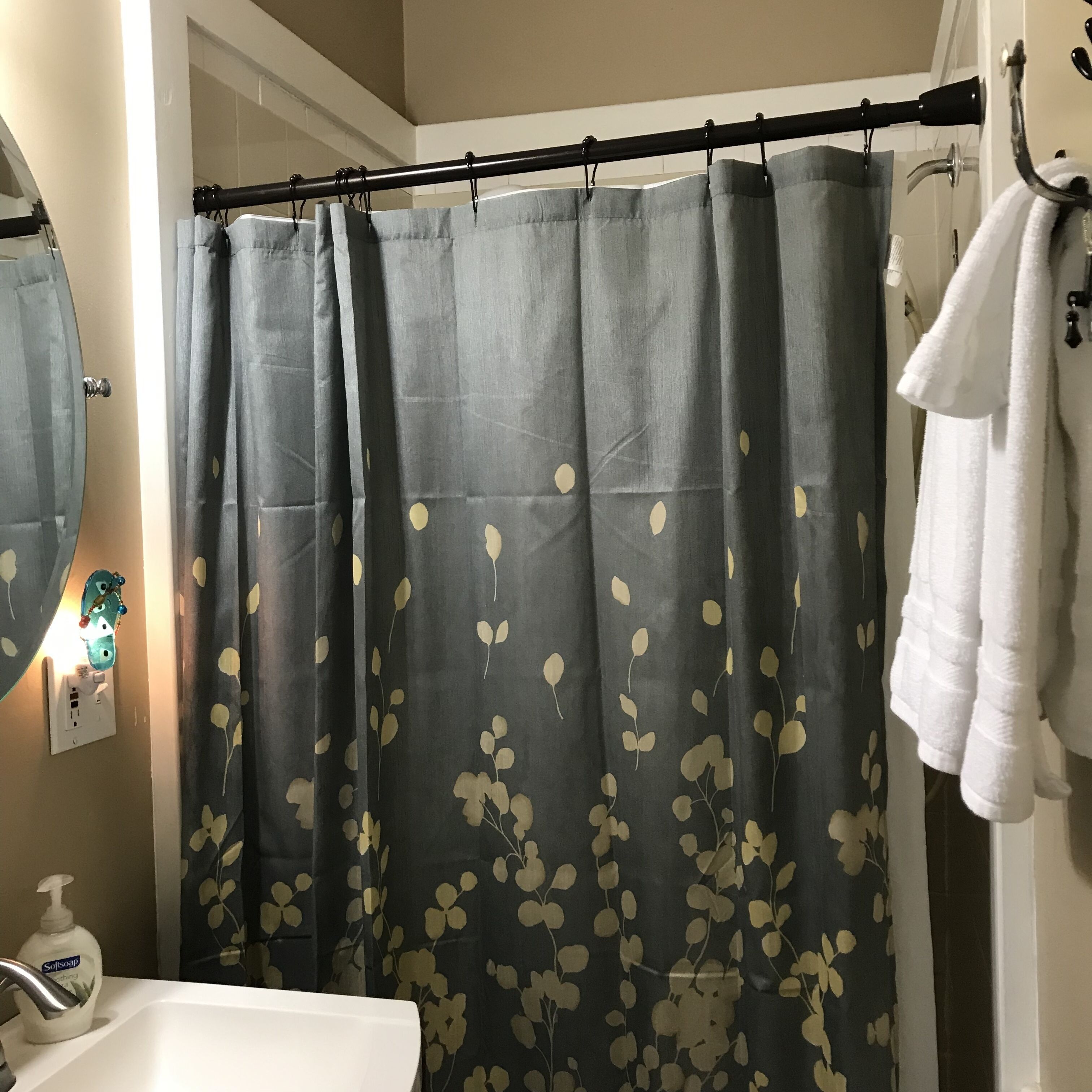 A bathroom with a shower curtain featuring a leaf pattern, a white sink, a soap dispenser, and a towel rack with a white towel.
