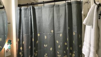 A bathroom with a shower curtain featuring a leaf pattern, a white sink, a soap dispenser, and a towel rack with a white towel.