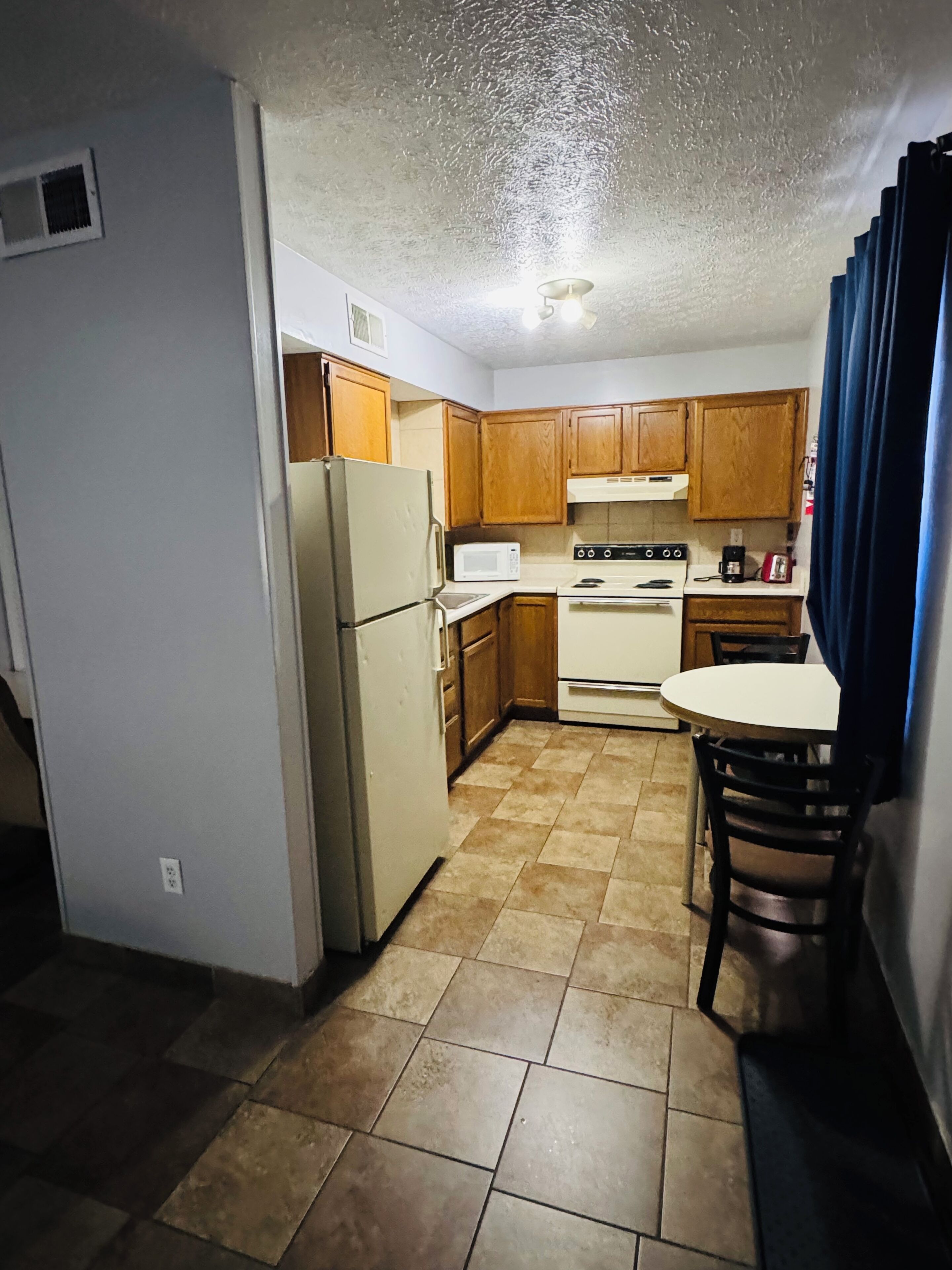 A compact kitchen with a refrigerator, microwave, stove, and wooden cabinets.
