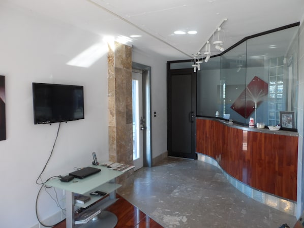 A modern interior with a curved reception desk, a mounted flat-screen TV, and a glass partition.