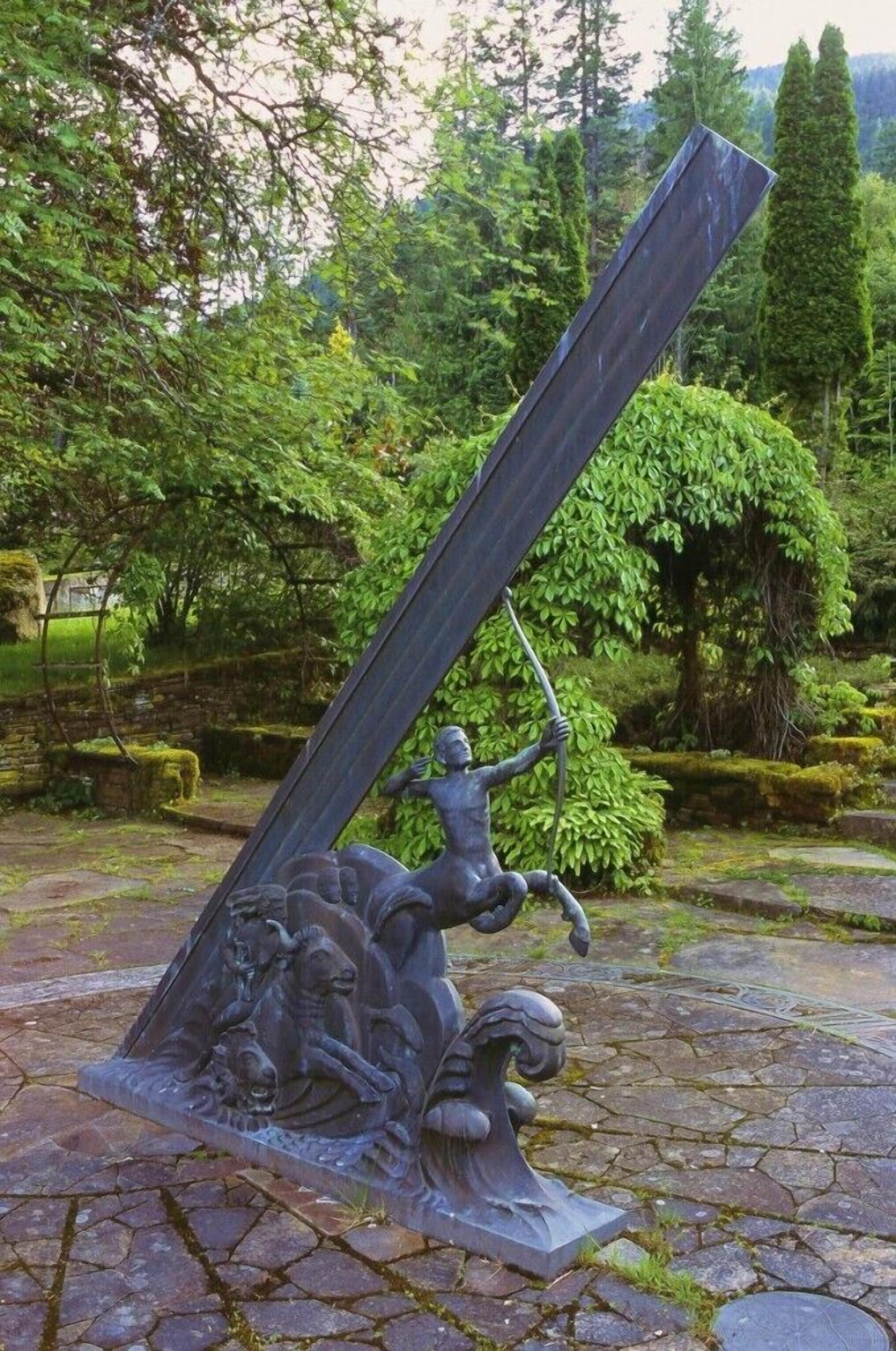 A sculpture of a figure with a spear, set on a stone base, surrounded by greenery.