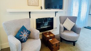 A living room with two armchairs, a flat-screen TV, a fireplace, and a large window.