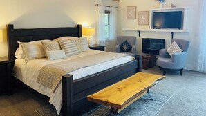 A bedroom with a bed, bedside tables, a TV, a fireplace, and a chair.