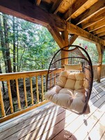 Una terraza de madera con una silla colgante y vistas al bosque.
