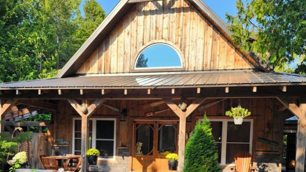 A rustic wooden cabin with a pitched roof, a covered porch, and a stone pathway leading to the entrance.