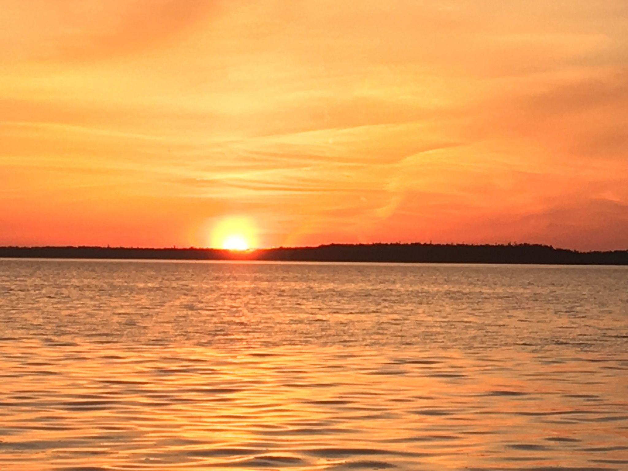 A sunset over a calm body of water with a distant shoreline.