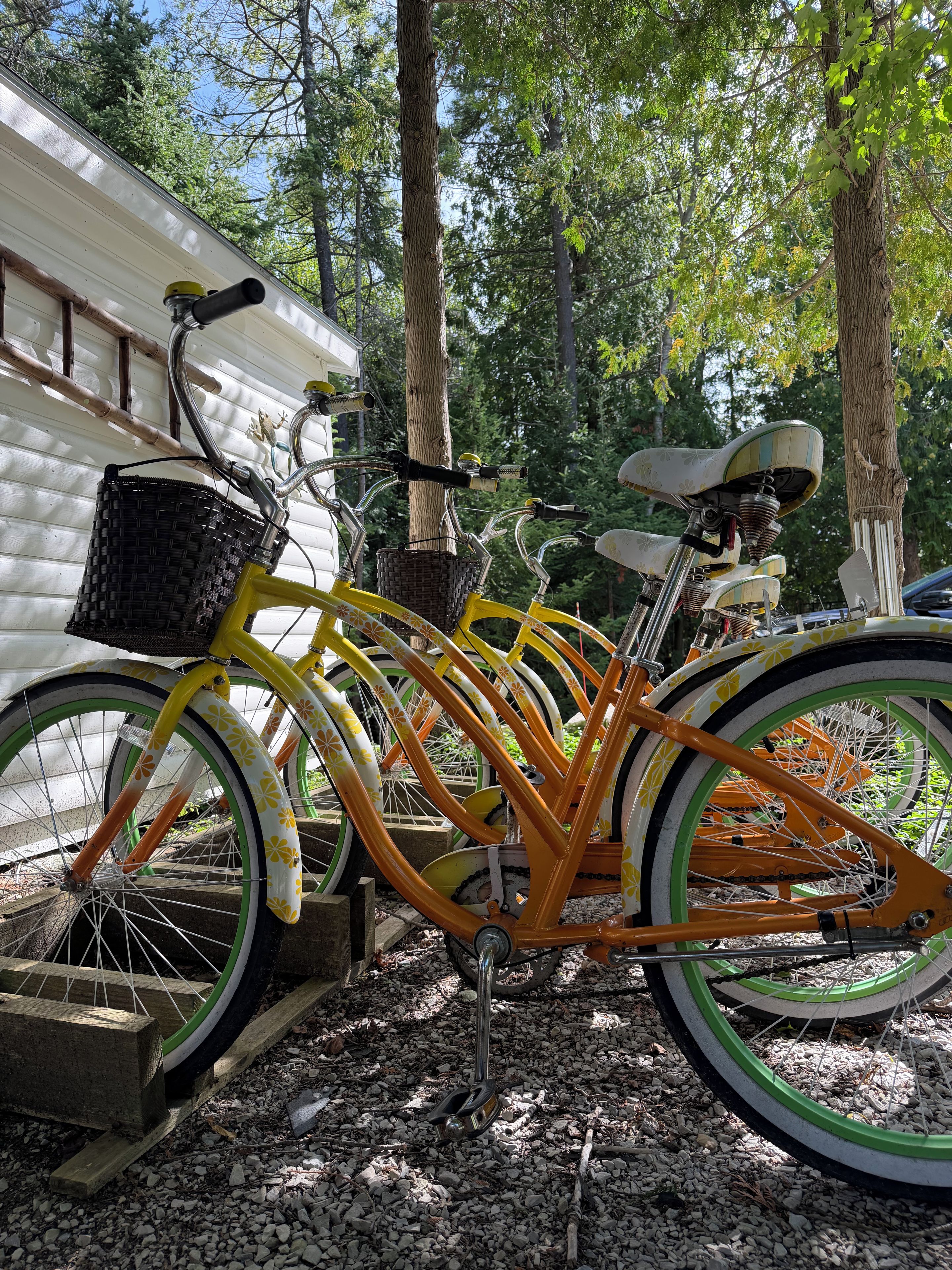 A yellow bicycle with a basket and a seat, parked on a gravel surface.