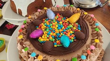 A variety of cakes and pastries on display, including a chocolate cake with colorful decorations and a white cake with orange icing.