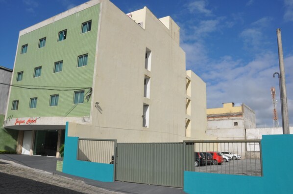 Un hôtel à la façade verdoyante et à la partie beige, doté d’une entrée fermée par un portail et d’un espace de stationnement bien visible.