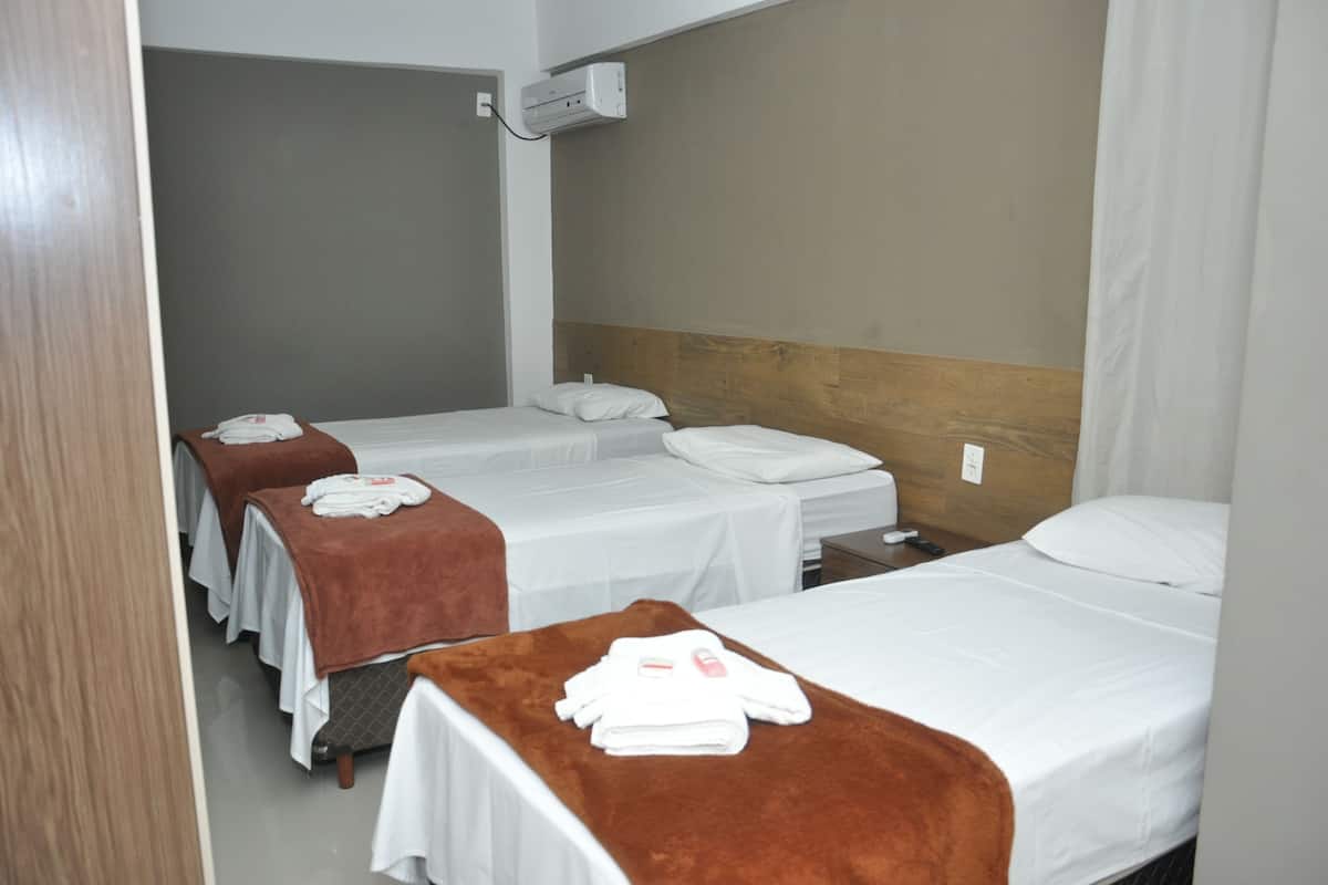 A hotel room with three single beds, each with a brown blanket and white towels.