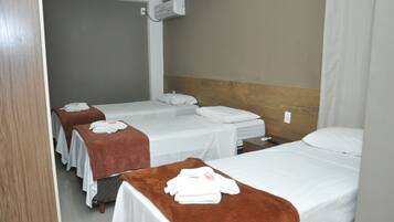 A hotel room with three single beds, each with a brown blanket and white towels.
