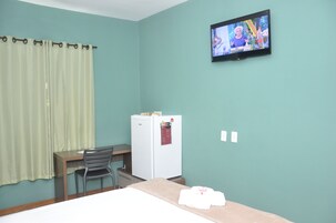 Una habitación con paredes color esmeralda, una cama, un escritorio con una silla, un refrigerador blanco y un televisor en la pared.