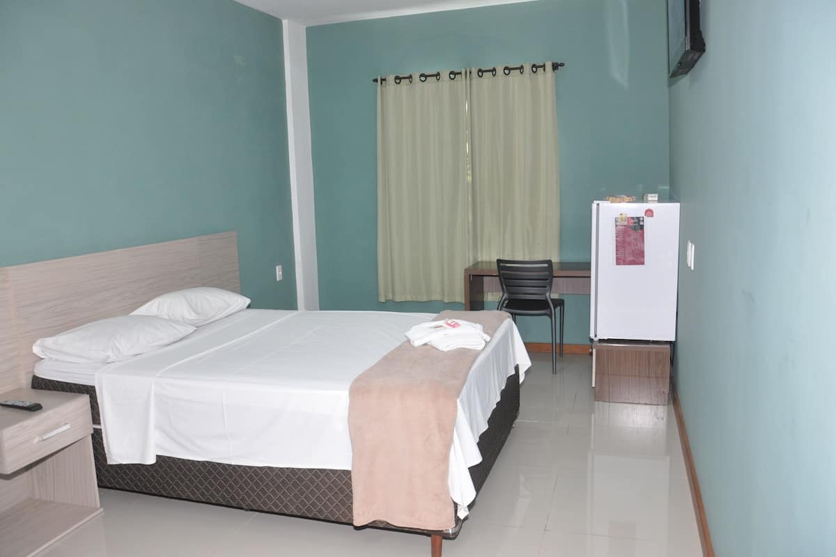 A hotel room with a bed, a desk, a chair, and a refrigerator.
