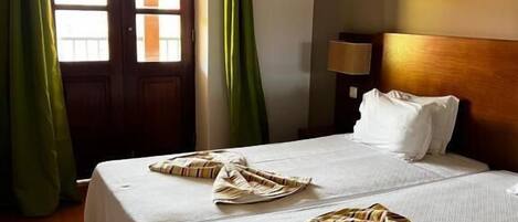 A hotel room with two beds, a wooden headboard, a nightstand, and a window with curtains.