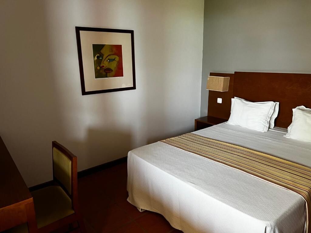 Een hotelkamer met een groot bed, een stoel, een nachtkastje en een lijst aan de muur.