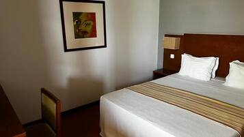 Een hotelkamer met een groot bed, een stoel, een nachtkastje en een lijst aan de muur.