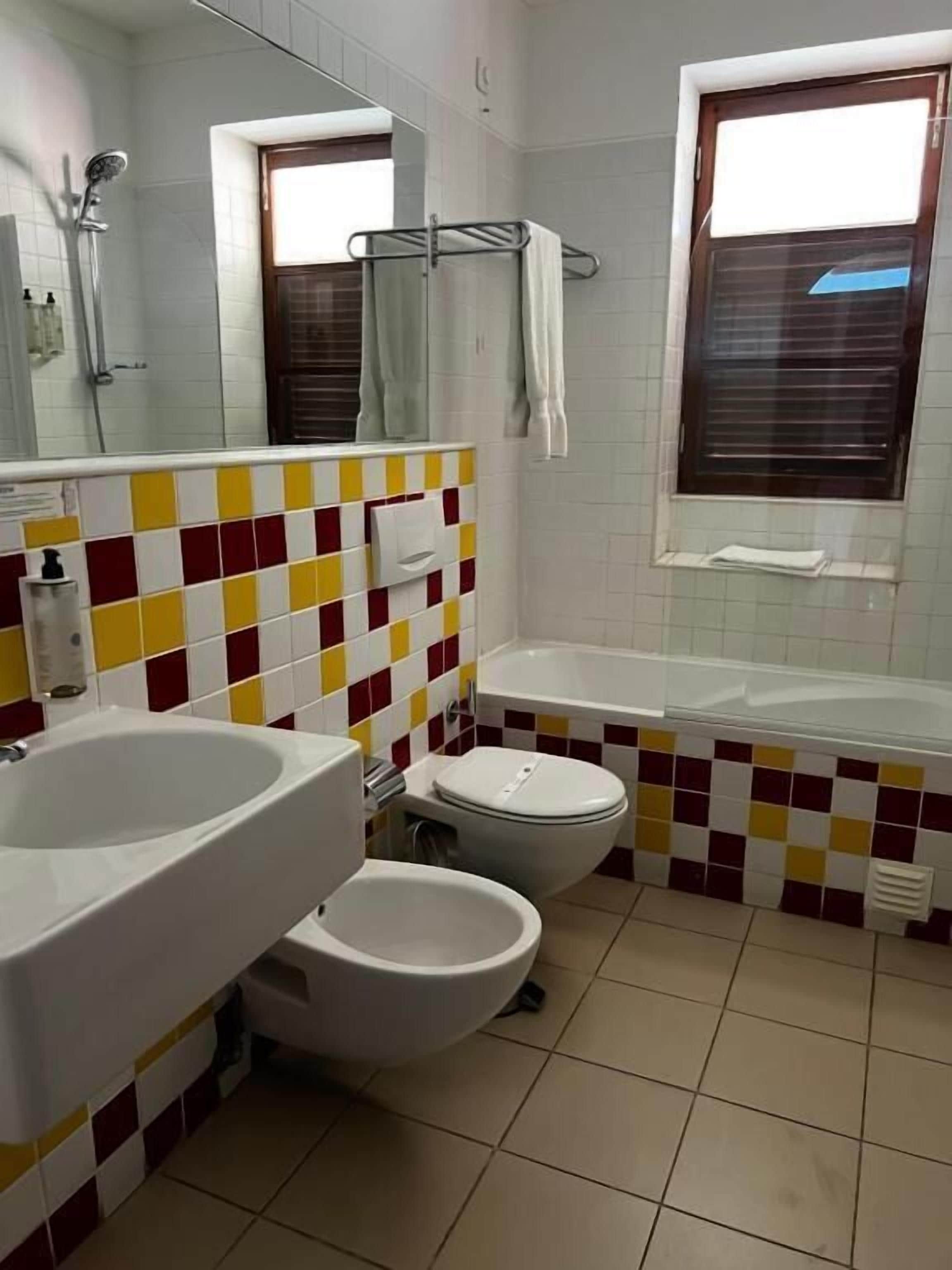 A bathroom with a large sink, toilet, and bathtub. There is a window with blinds and a mirror above the sink.
