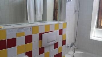 A bathroom with a white sink, toilet, and shower. The walls are tiled in a red and yellow pattern.