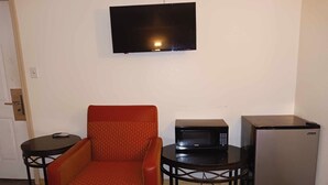 A small room with a single orange chair, a black table with a microwave, and a refrigerator. - HomeTown Inn By OYO Lakin, KS (Lakin)