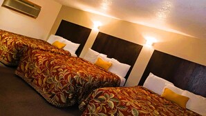 A hotel room with three beds, each with a patterned bedspread and white pillows. There is a wall-mounted air conditioner and two wall-mounted lights. - HomeTown Inn By OYO Lakin, KS (Lakin)
