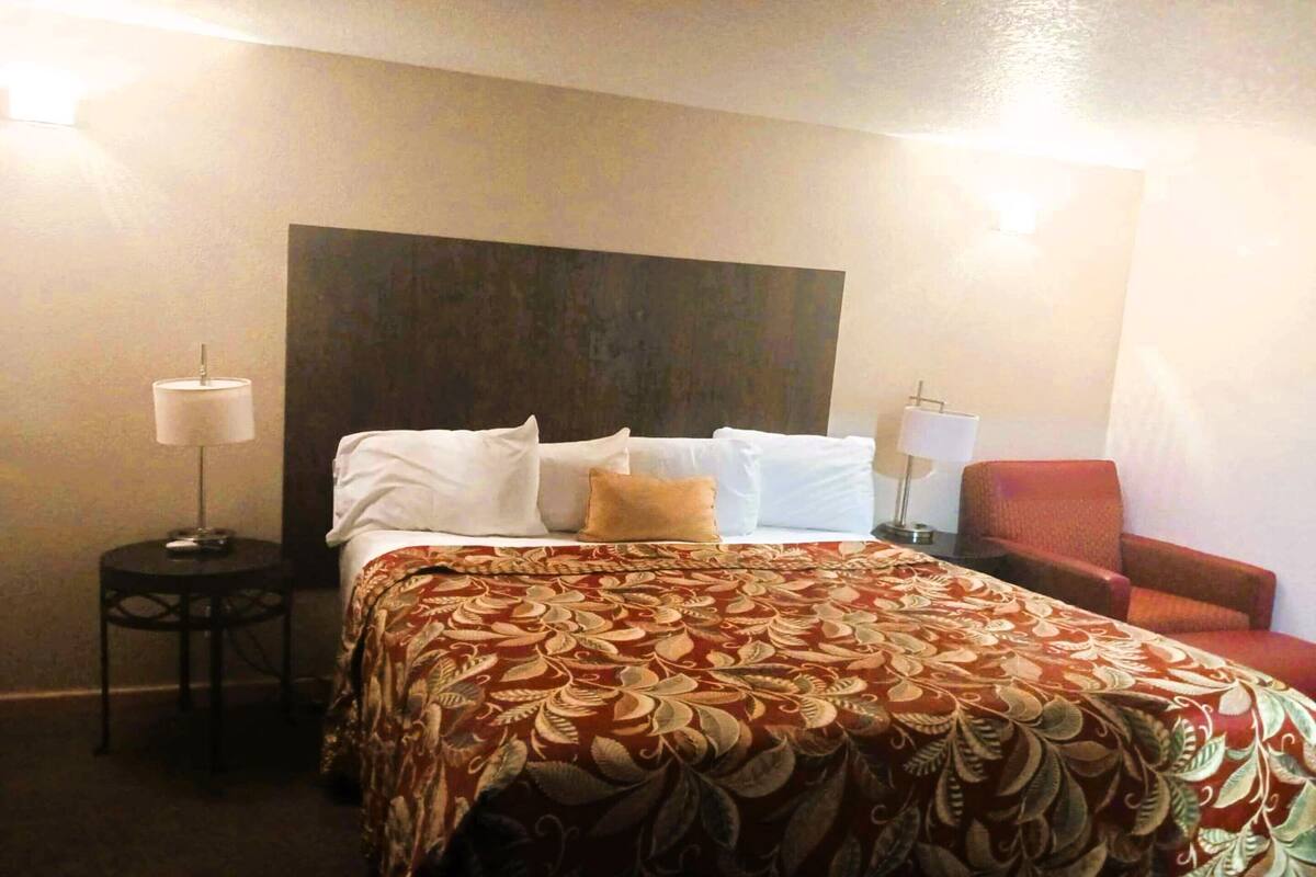 A hotel room with a large bed, a red chair, and two bedside lamps.